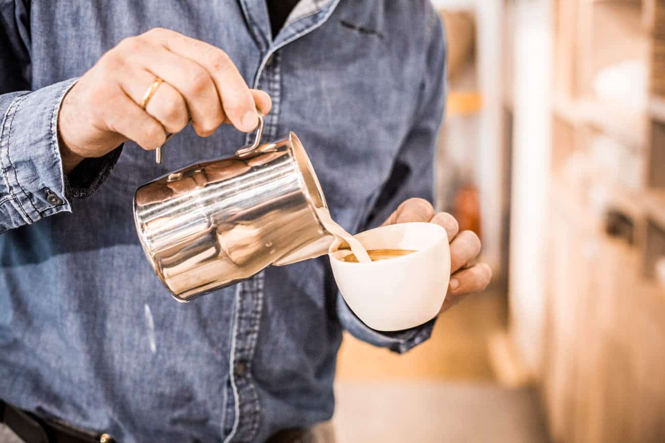 mann gießt milch in kaffeetasse